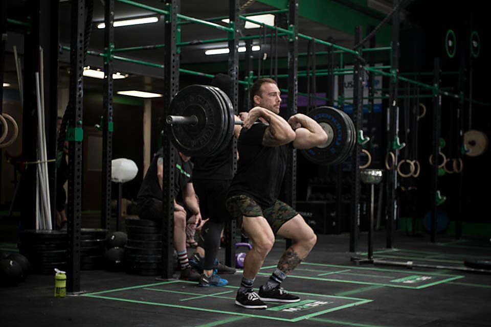 A man performs a front squat with a barbell in a gym setting.