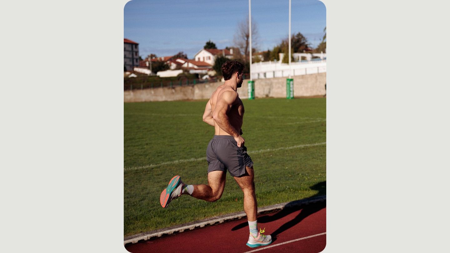 A shirtless man with an athletic build runs along a track on a sunny day.