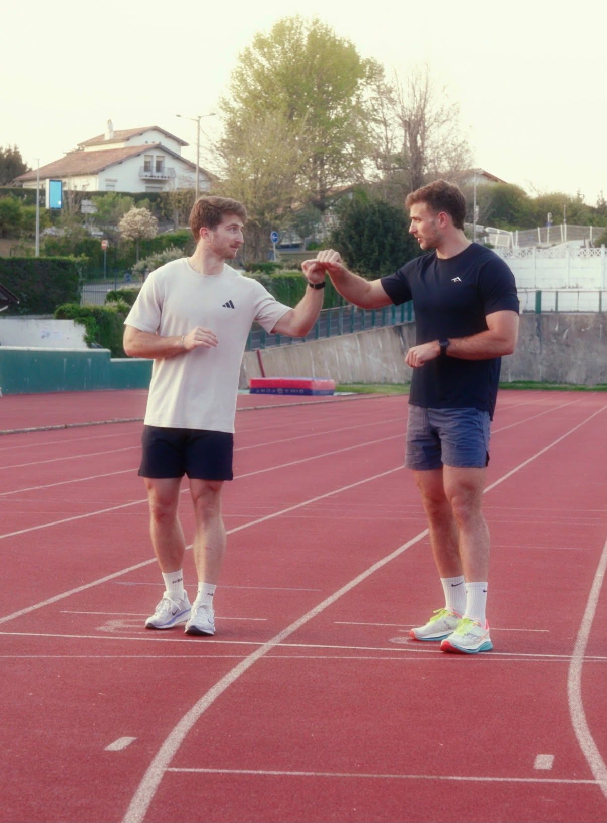 Two men in athletic wear fist bump while standing on an outdoor running track.