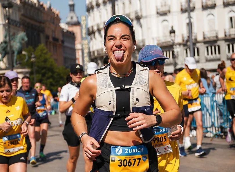 A female runner with a playful expression sticks her tongue out while participating in a crowded city marathon.