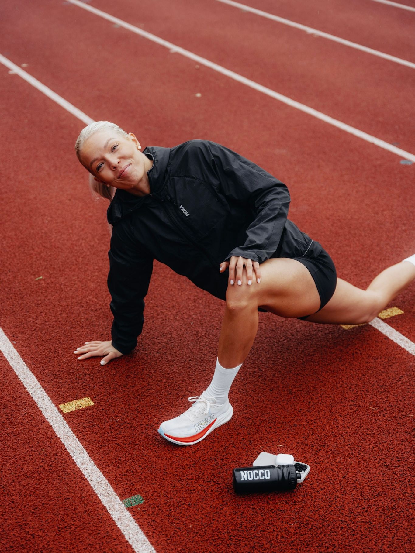 A woman in athletic wear performs a lunge stretch on a red running track.