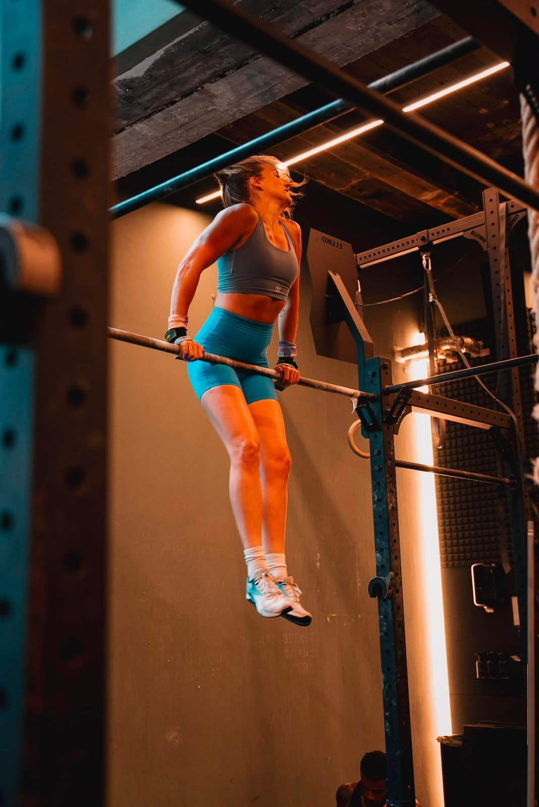 A woman in athletic wear performs a bar dip exercise in a dimly lit gym.