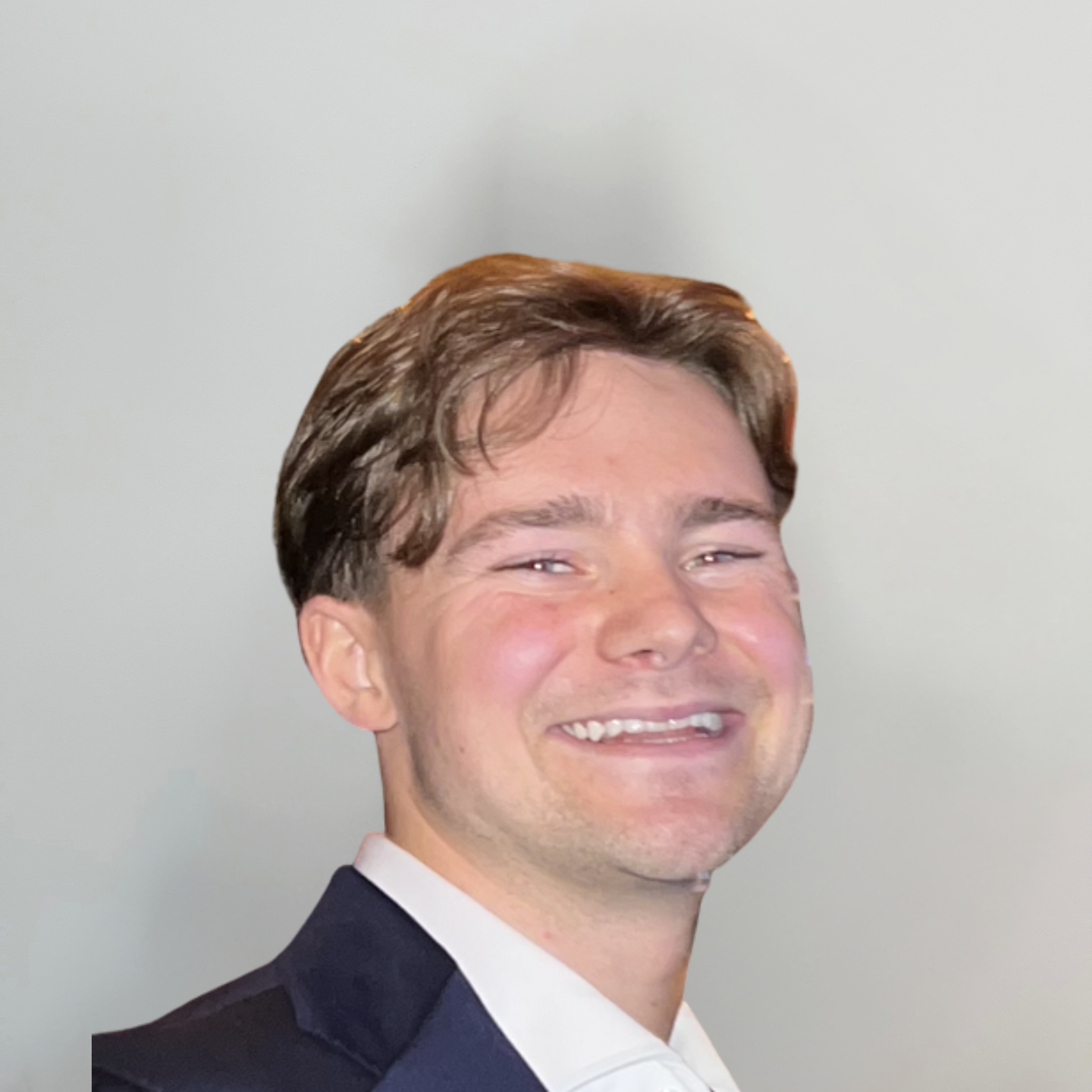 A young man with brown hair smiling while wearing a dark suit jacket and white shirt against a plain background.