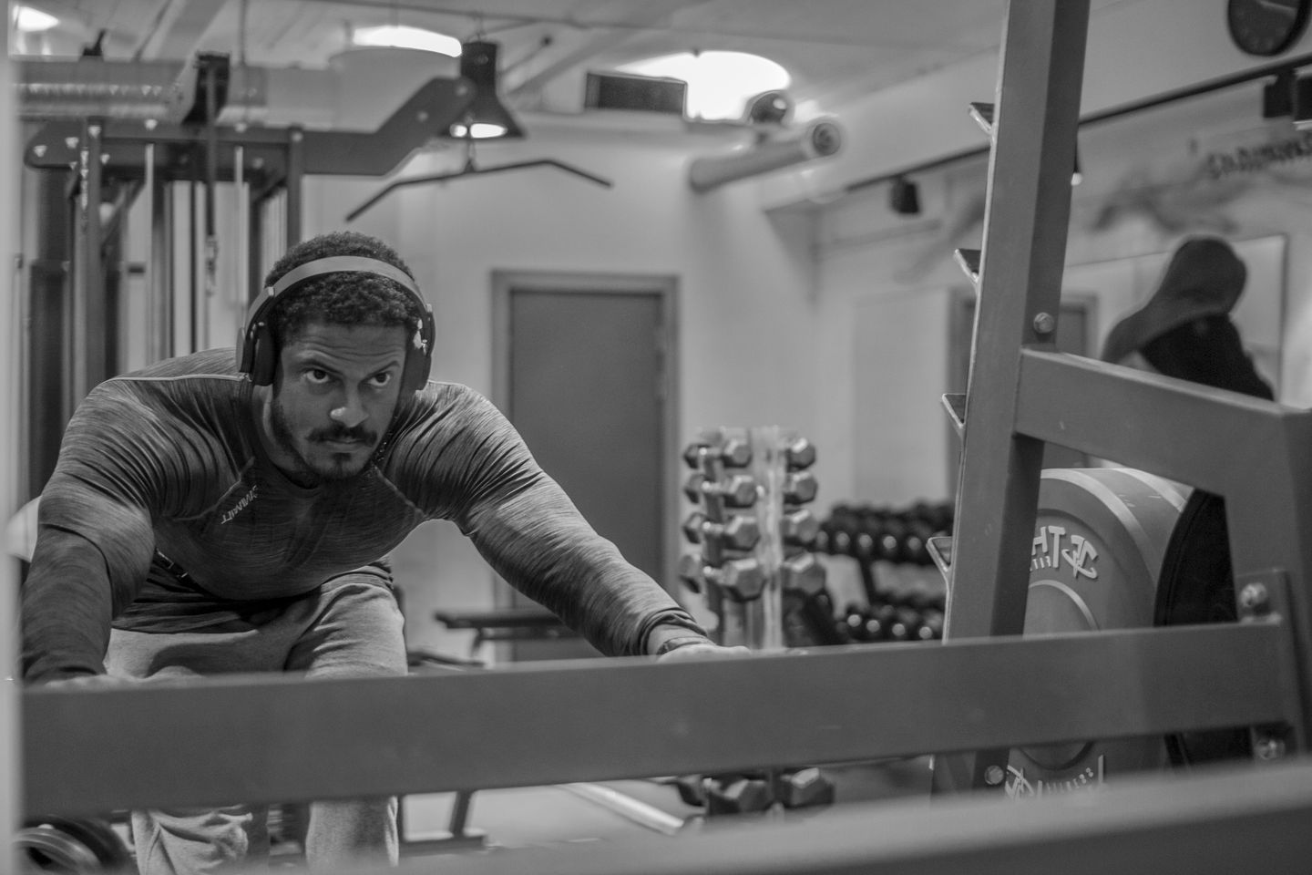 A focused man wearing headphones performs a rowing exercise on a machine in a gym.