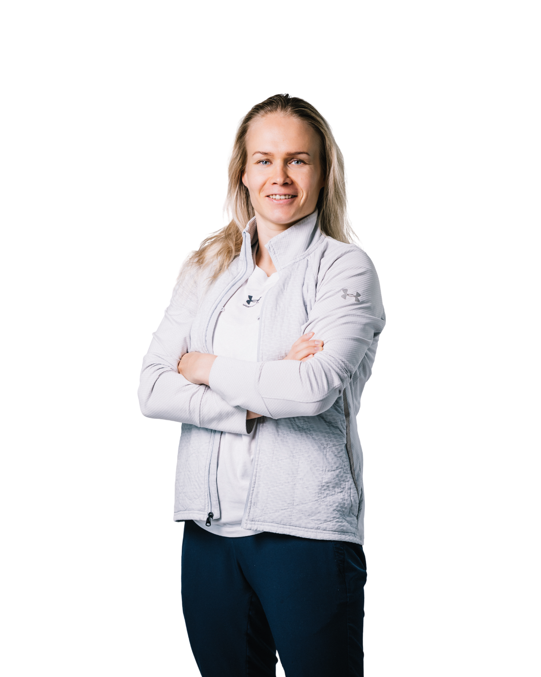 A blonde woman in a light grey athletic jacket stands with her arms crossed against a white background.