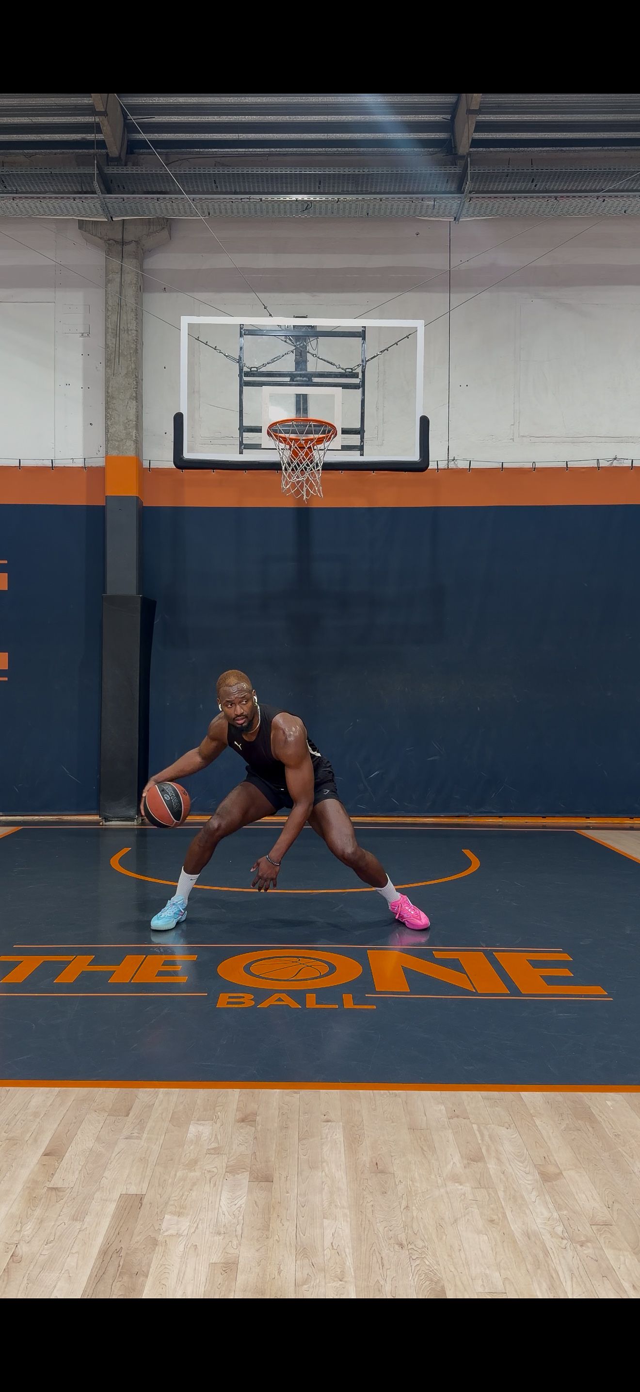 A basketball player in a low defensive stance dribbling a ball on an indoor court.