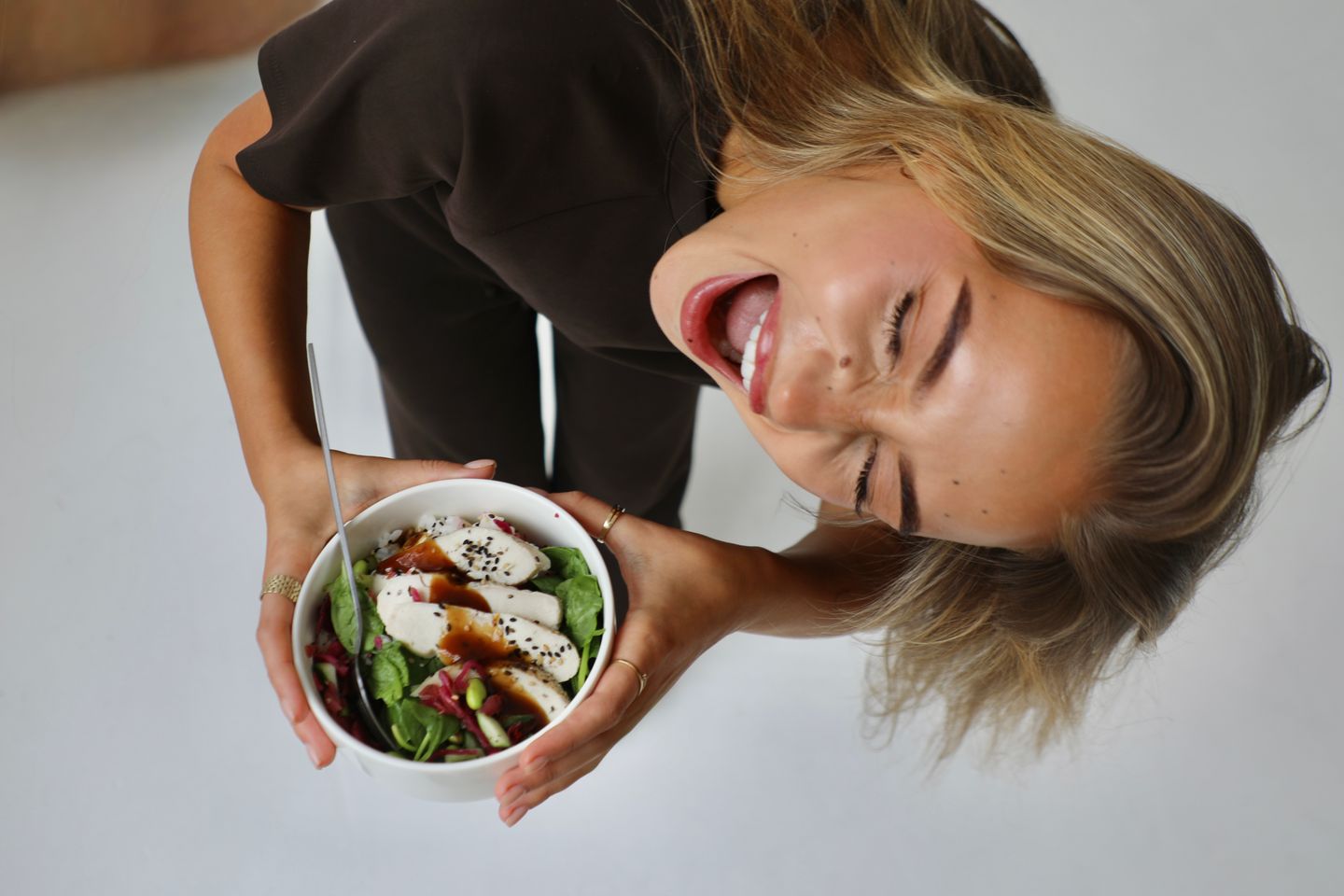 A woman leans over a bowl of chicken and vegetable salad with an excited expression.
