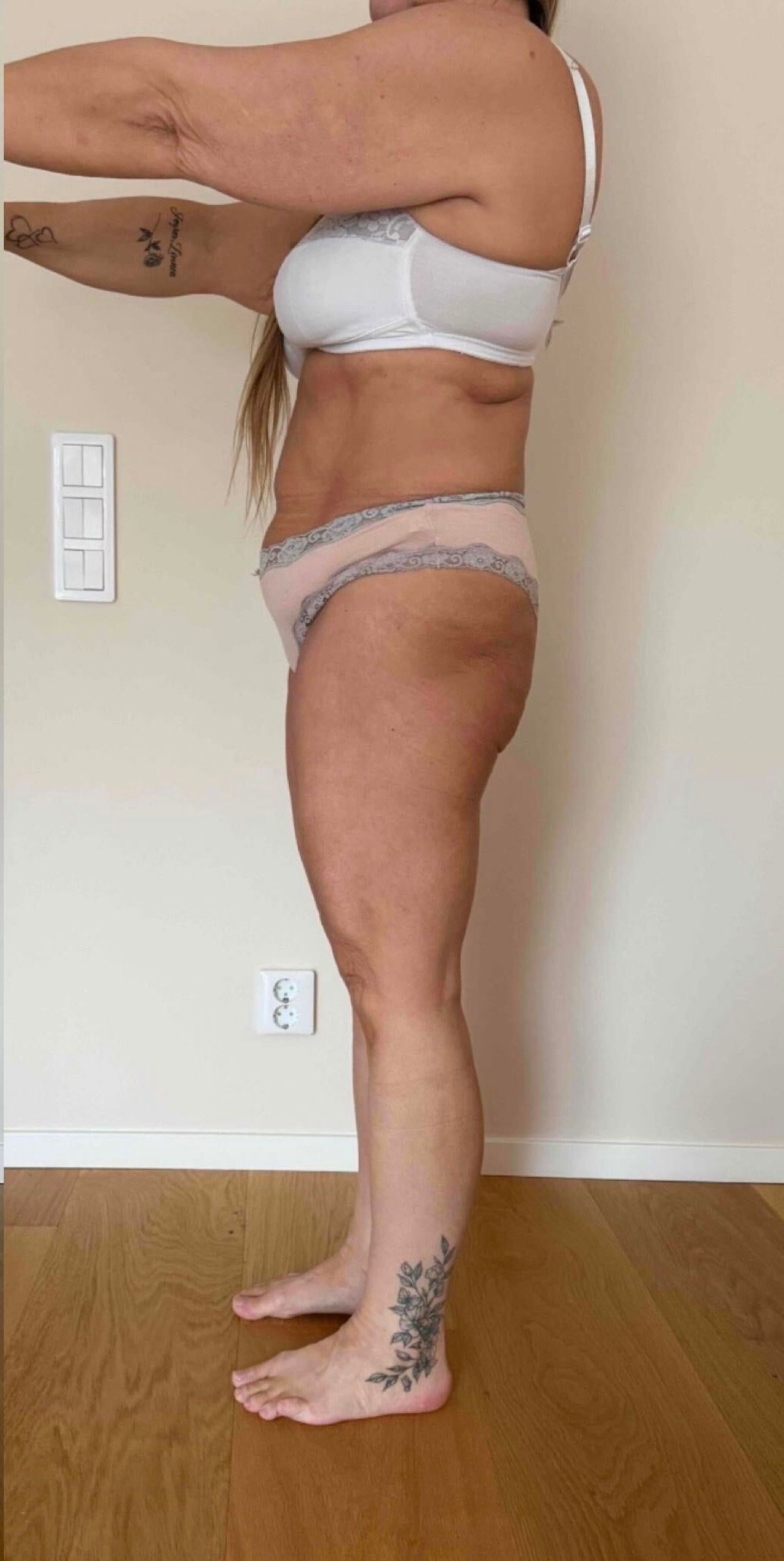 A person stands in profile against a plain wall, wearing undergarments and holding their arms extended forward.