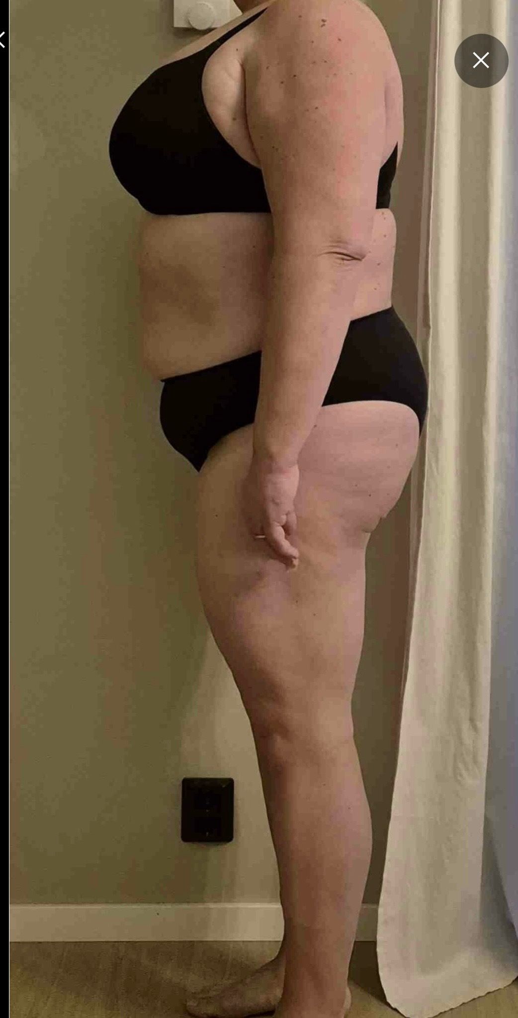 A person stands in profile wearing black undergarments for a fitness progress check.
