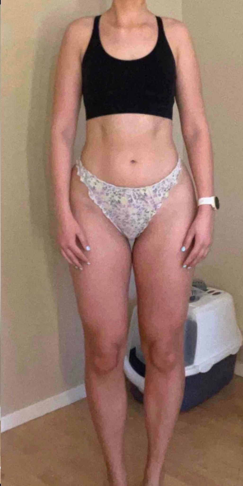 A person stands facing forward in a black sports bra and patterned underwear to show their physique.