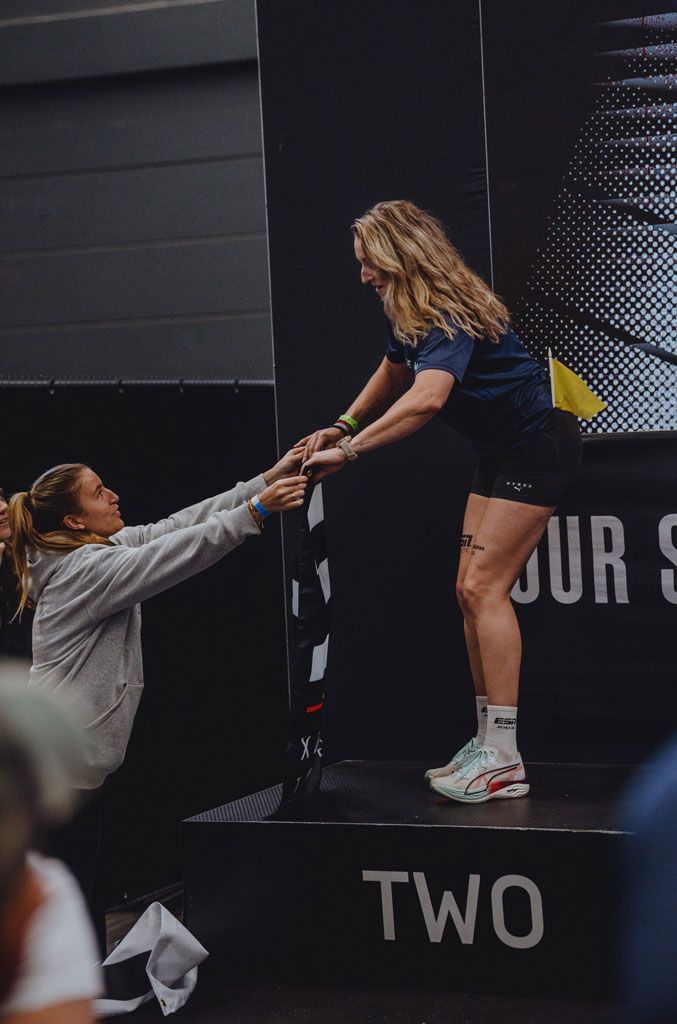 Een coach op een podium wordt geholpen door een vrouw tijdens een fitnessevenement.