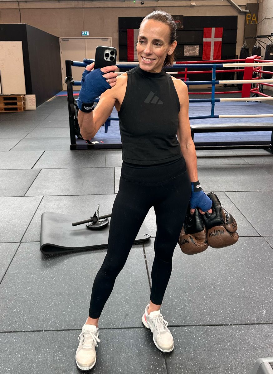 Coach Camilla in gym wear and hand wraps, holding boxing gloves for a selfie.