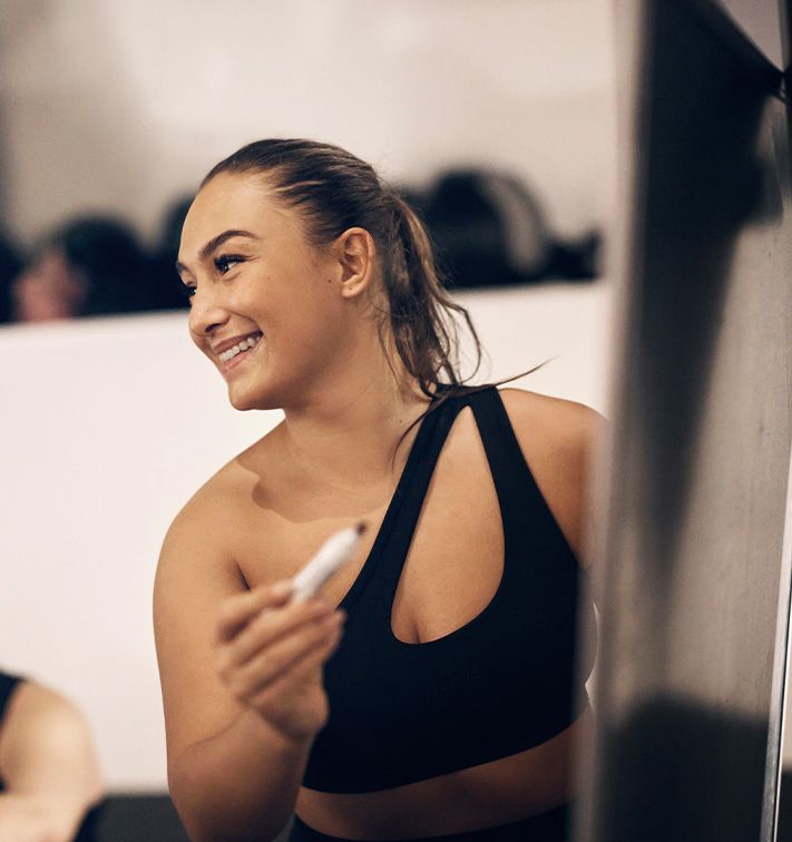 Coachen smiler i et fitnesscenter med en telefon i hånden