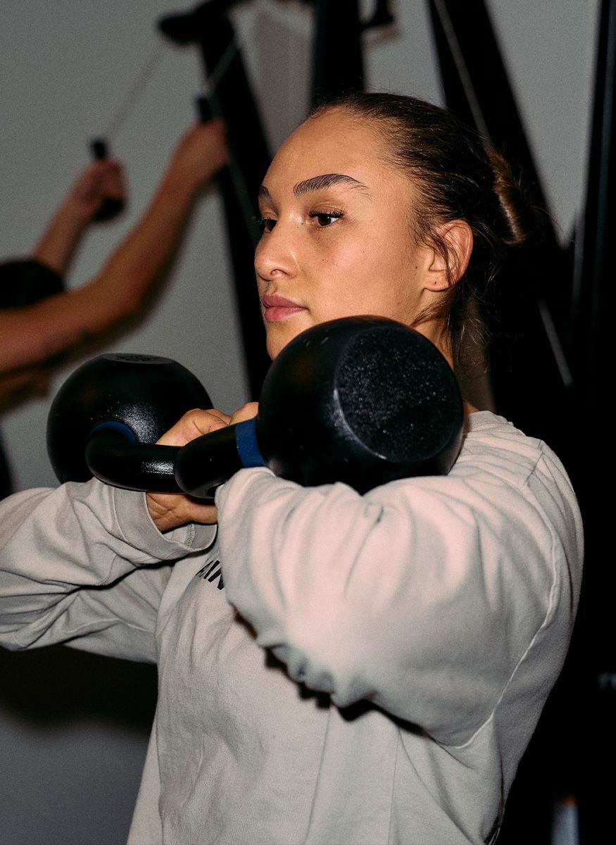 Coachen løfter to kettlebells i brysthøjde i et fitnesscenter