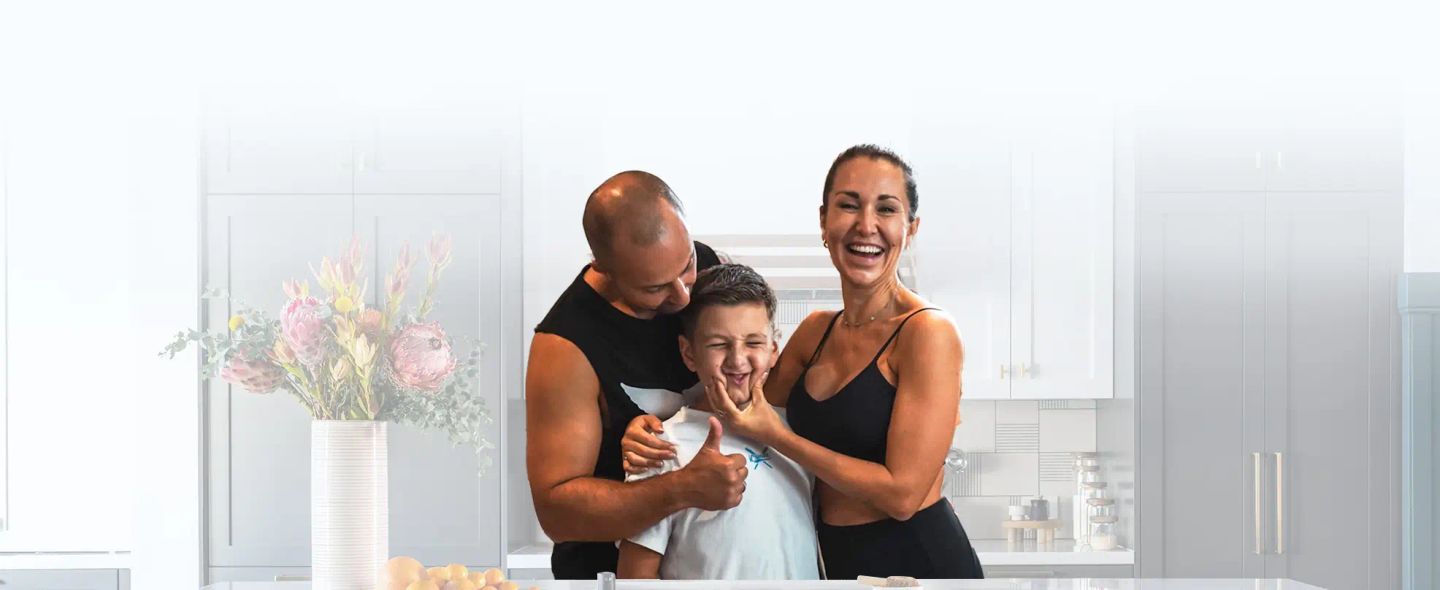 Anna lacht mit ihrem Sohn und ihrem Partner in der hellen Familienküche