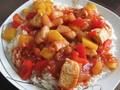 A plate of sweet and sour chicken with pineapple and bell peppers served over white rice.