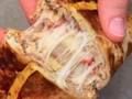 Hands pulling apart a warm pastry to reveal melted, stretchy cheese inside.