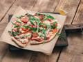 A freshly baked pizza topped with arugula and tomatoes served on a wooden board.
