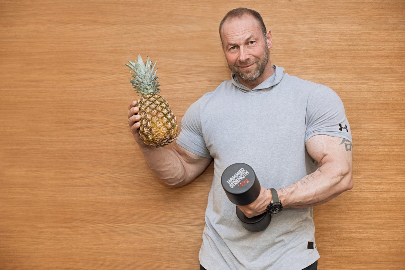 Matthias Botthof mit Hantel und Ananas, Portrait vor Holzwand