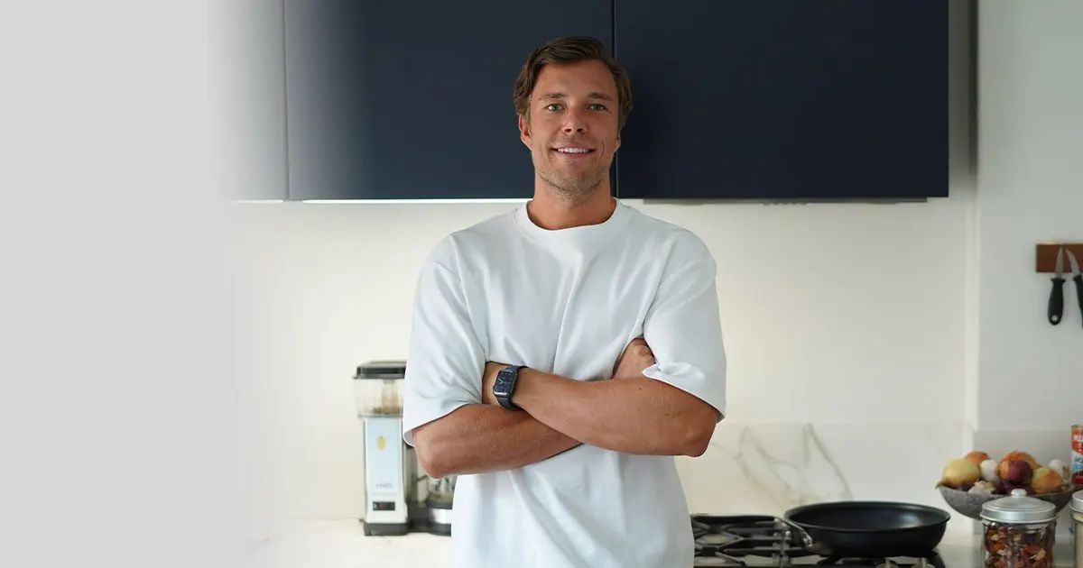 Coach Anthon Hellman står med armarna i kors i ett kök med frukt och stekpanna i bakgrunden